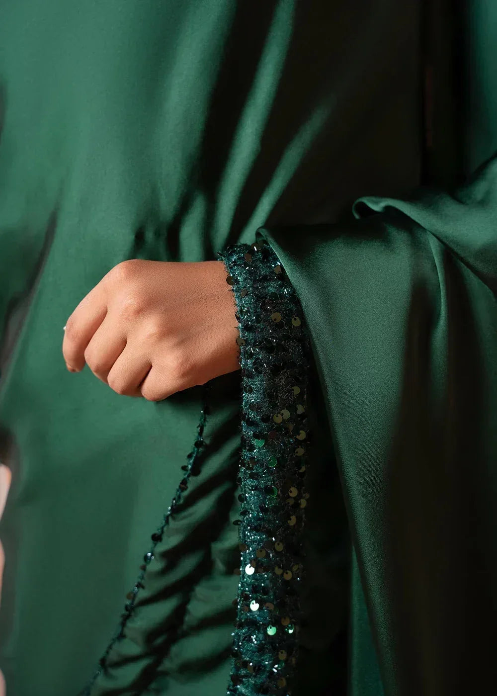 Close-up of a hand holding green satin fabric with sequin embellished border, elegant textile