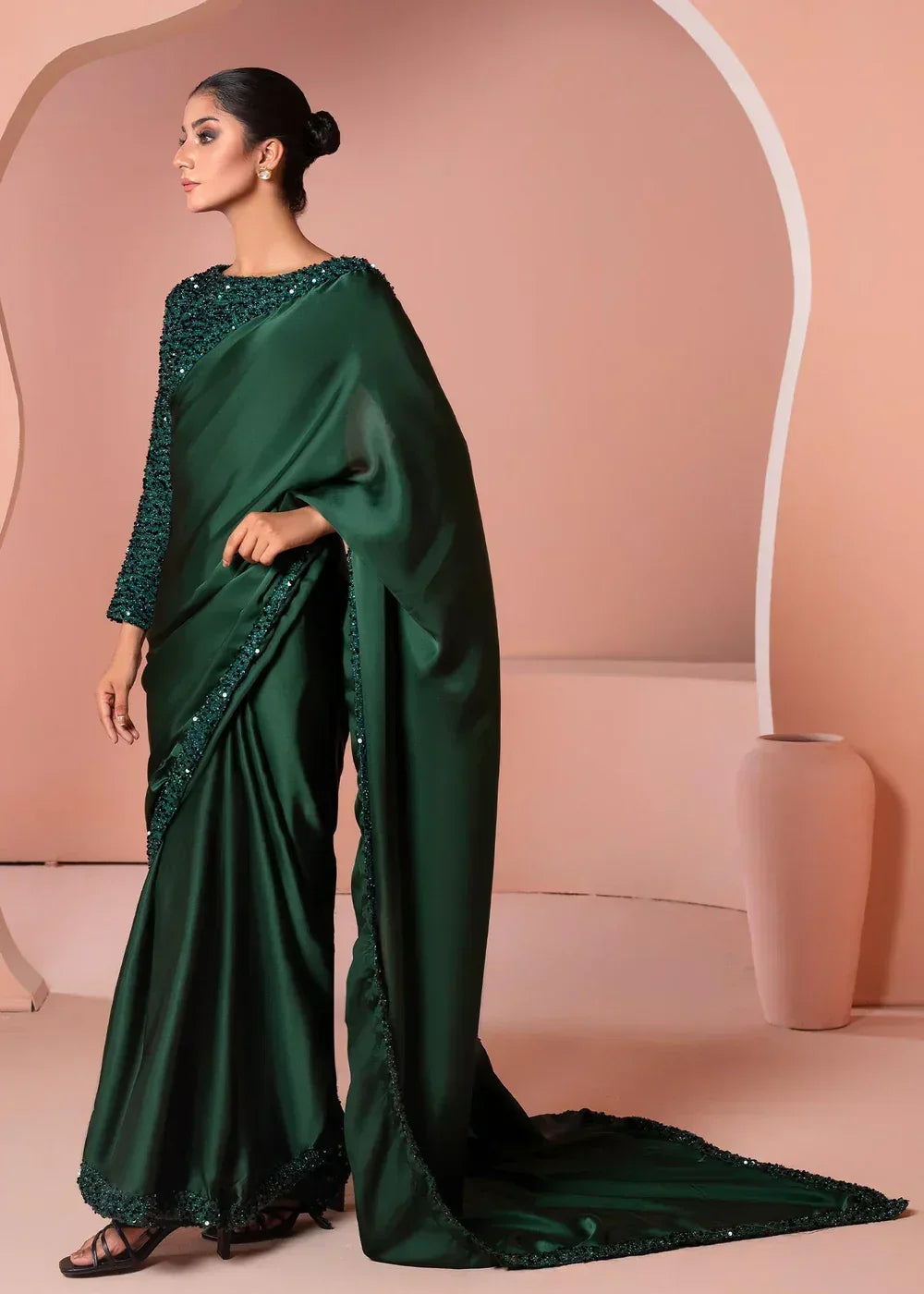 Woman in elegant dark green satin saree with sequin details, standing in a minimal studio.