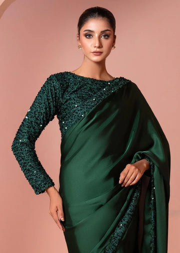 Woman in dark green sequin saree with long sleeves, posing against a pink background