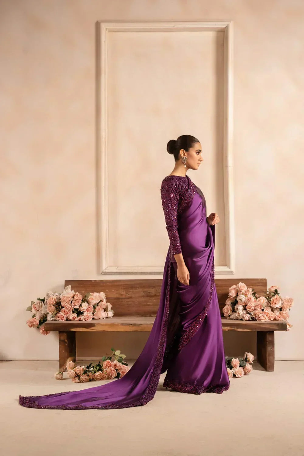 Woman in elegant purple sequin saree with long train, posed indoors by pink roses
