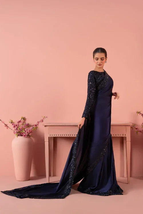 Woman in elegant navy blue sequin gown with long train, standing by pink table and vases