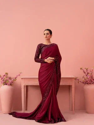 Woman in elegant maroon saree with sequin details standing in pink floral setting