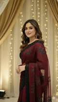 Woman wearing an elegant maroon saree with black floral embroidery at a festive indoor event