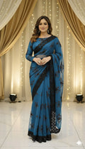 Woman wearing elegant blue saree with black lace, standing in front of draped curtains and lights