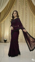 Woman in elegant maroon saree with black embroidery, standing against draped curtains and string lights