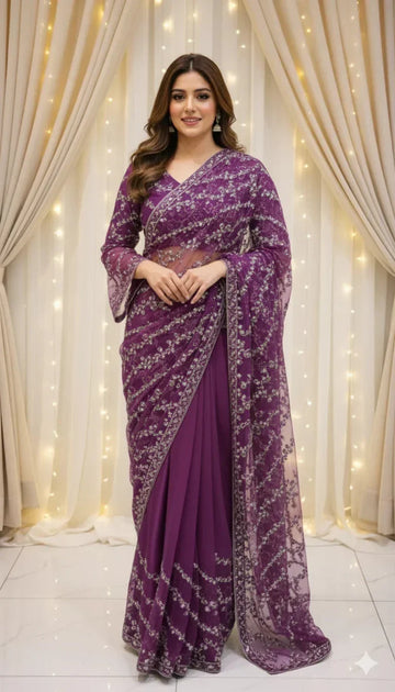 Woman in a purple embroidered saree posing indoors with curtain and string lights backdrop