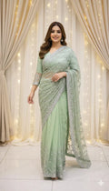 Woman in pastel green sequin saree standing in front of draped curtains and fairy lights