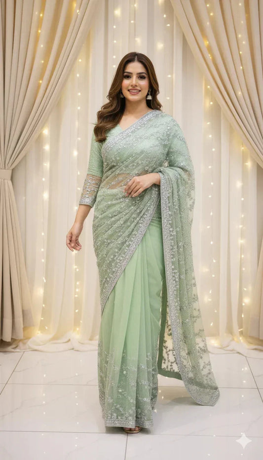 Woman in pastel green sequin saree standing in front of draped curtains and fairy lights