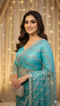 Woman in turquoise embroidered saree holding clutch, smiling in festive setting for Sareeium jan
