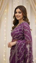 Smiling woman in a purple embroidered saree with wavy hair, standing by cream curtains, Sareeium jan