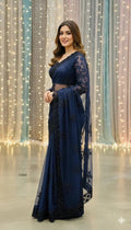 Woman in elegant navy blue saree with lace details, standing indoors with fairy lights backdrop