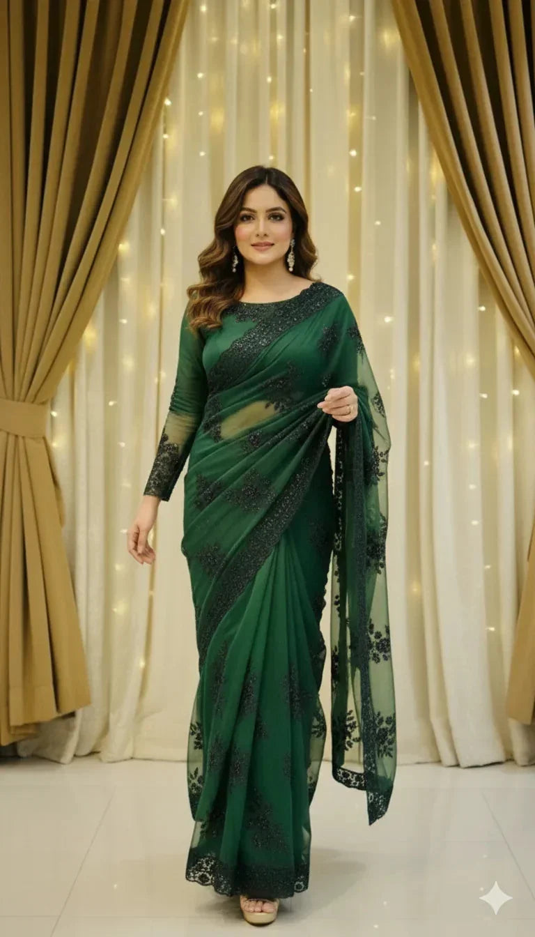 Woman in elegant green saree with black embroidery, standing indoors with curtains and lights