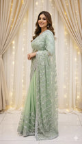 Woman in mint green embroidered saree standing indoors with curtain and fairy lights backdrop