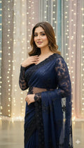 Woman wearing elegant navy blue embroidered saree, posing against festive lights backdrop