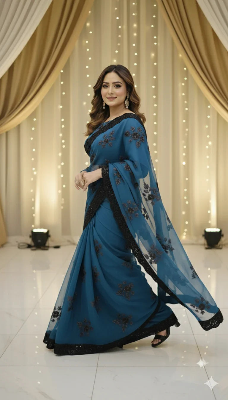 Woman in teal embroidered saree posing indoors with draped curtains and string lights
