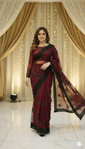 Woman in maroon designer saree with black embroidery, posing indoors with elegant drapes