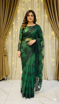 Woman in elegant green embroidered saree standing indoors with curtain and fairy lights background