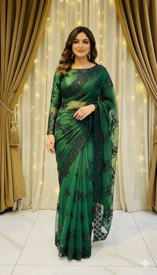 Woman in elegant green embroidered saree standing indoors with curtain and fairy lights background