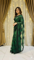 Woman in green embroidered saree posing indoors with beige curtains and string lights