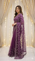 Woman in a purple embroidered saree standing by cream curtains with fairy lights, Sareeium jan