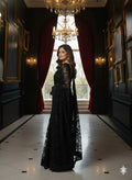 Woman in elegant black saree standing in a luxurious hallway with chandeliers and red curtains