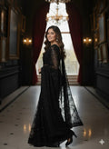 Woman in an elegant black saree with lace details stands in a luxurious chandelier-lit hallway