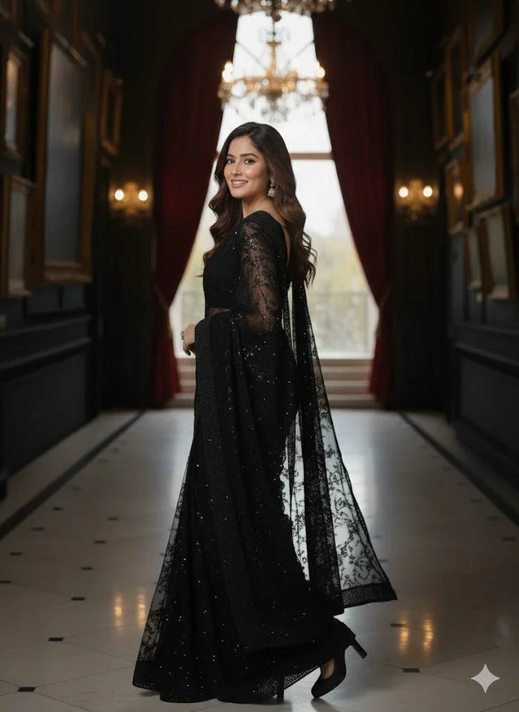 Woman in an elegant black embroidered saree posing in a grand, chandelier-lit hallway