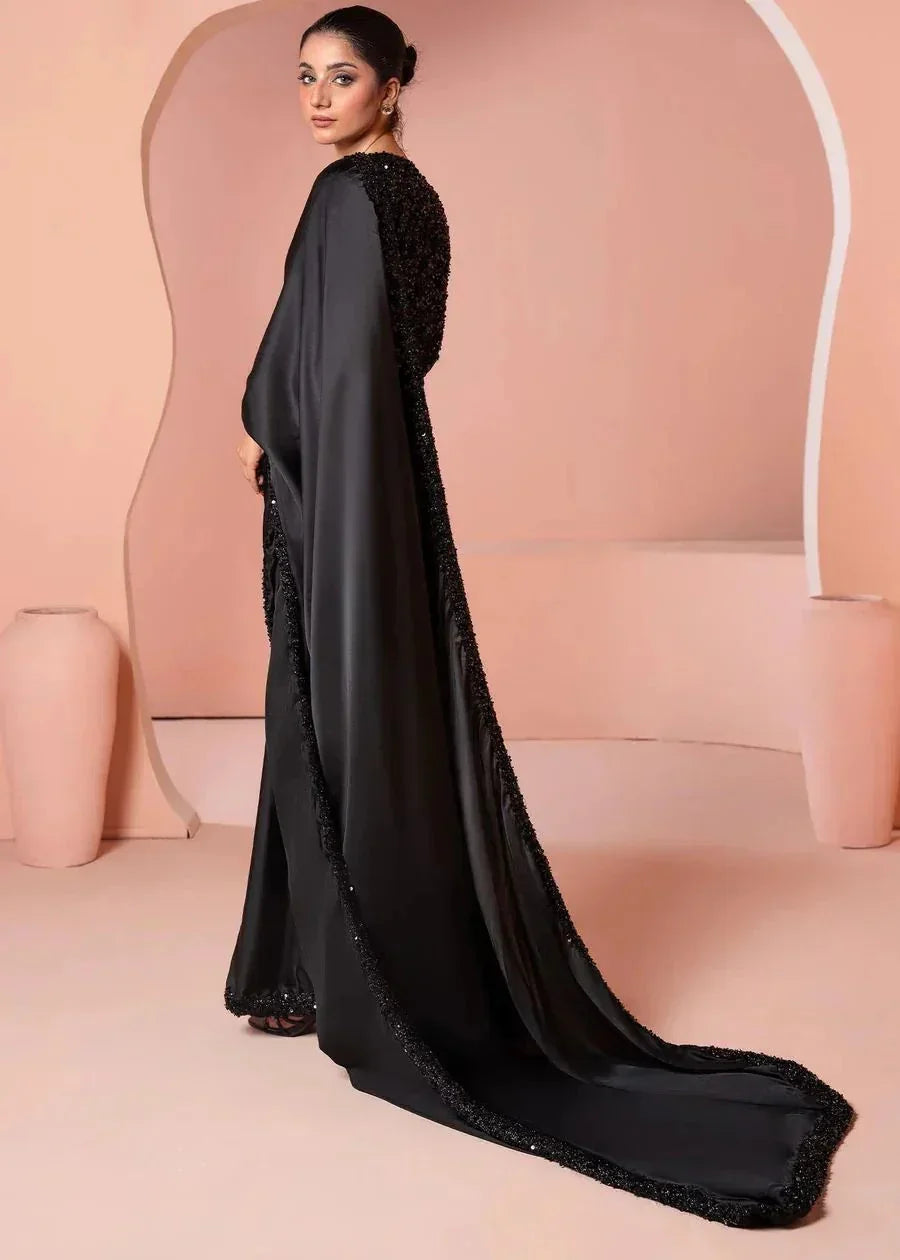 Woman in elegant black embellished saree with long drape, standing against peach backdrop