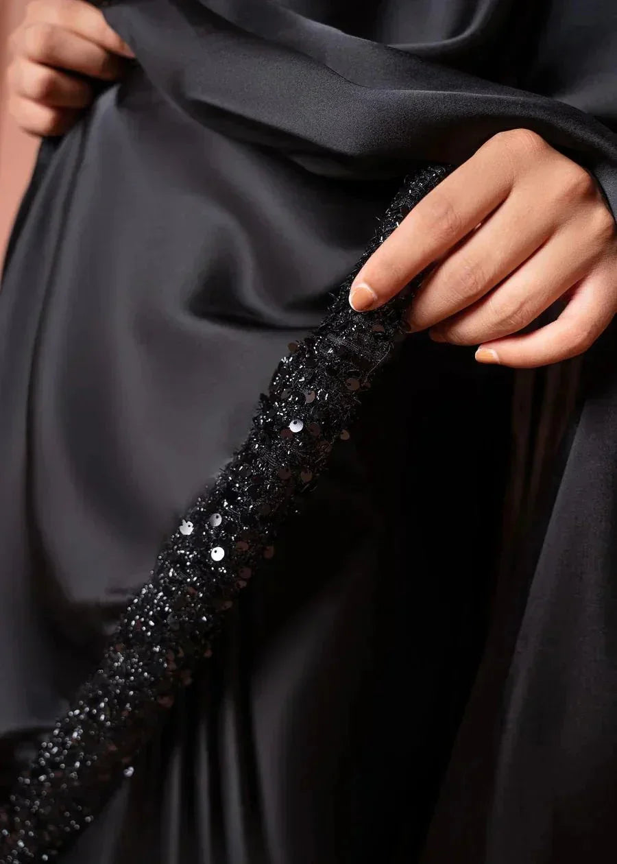 Hand holding black satin fabric with sequined, beaded trim detail, elegant textile closeup