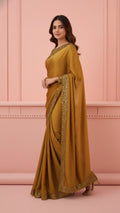 Woman in a mustard saree with sequin border, posing against a pink wall, Sareeium jan style