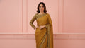 Woman in mustard yellow saree with gold sequin blouse, posing against a pink background