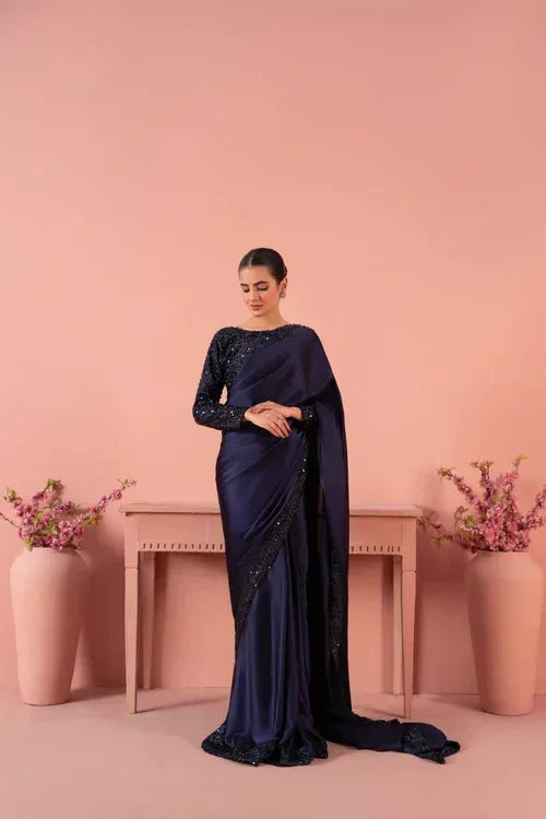 Woman in navy blue sequin sari standing indoors with pink vases and flowers