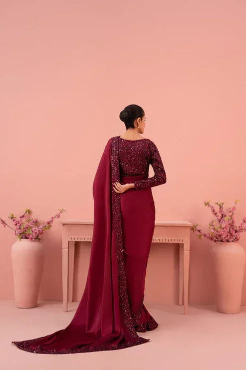 Woman in a deep maroon embellished saree standing in a pink room with floral vases